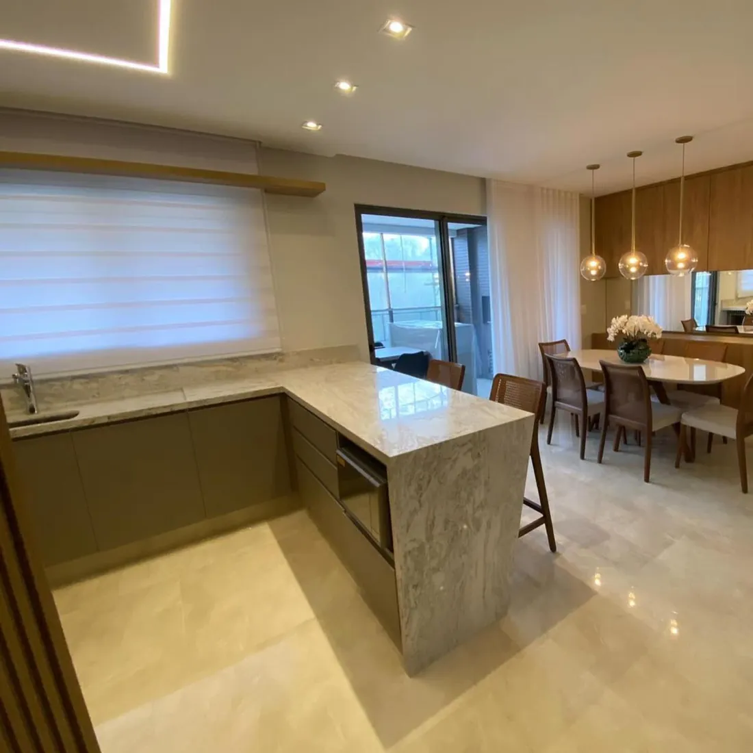 Bancada em pedra clara integrando cozinha e sala de jantar em apartamento de alto padrão