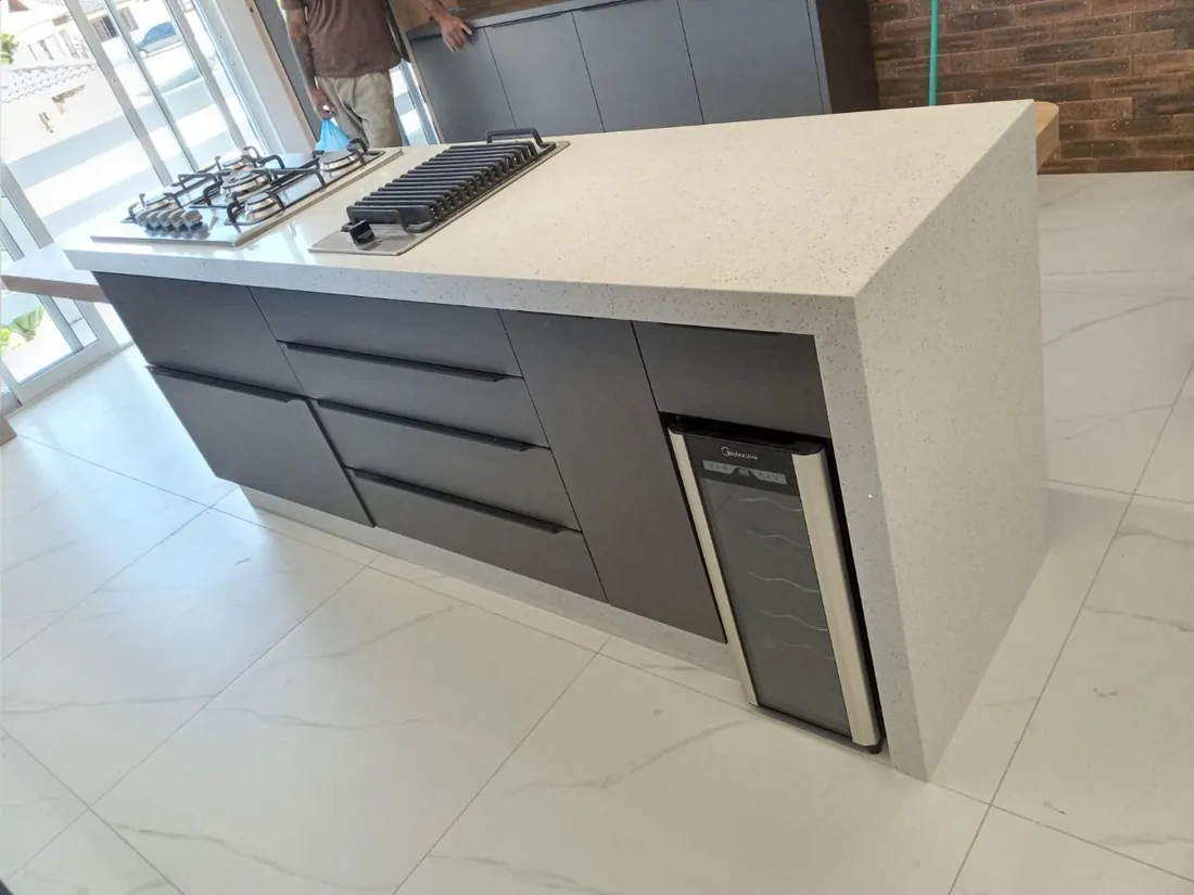 Cozinha ampla com ilha central em pedra clara e piso porcelanato