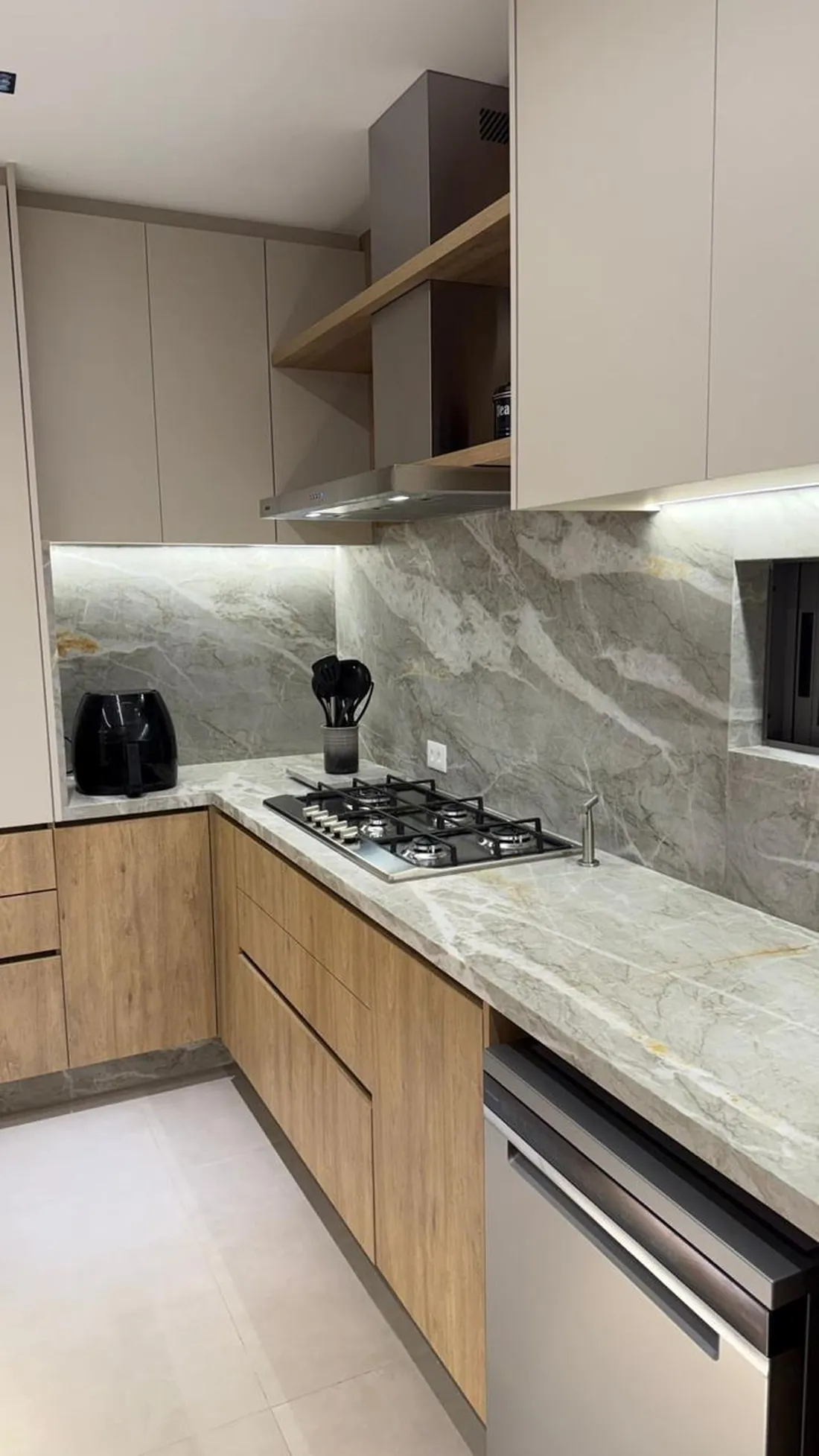 Bancada em pedra clara com marcenaria amadeirada e cooktop embutido